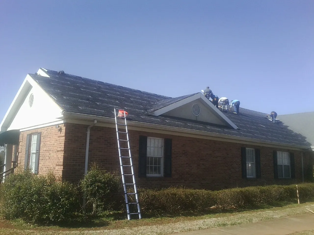 Crew tearing shingles off a brick ranch roof with a ladder set — Emergency Roof Repair work by our crew in Elliston