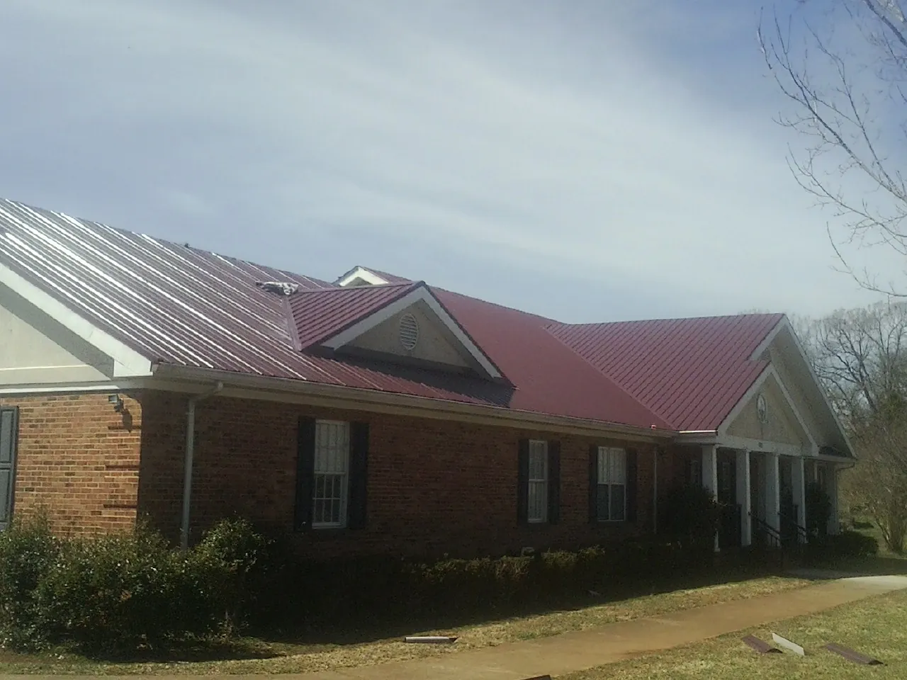 Red metal roof with gabled entries on a long brick building, from a Hail Damage Roof Repair job in Elliston