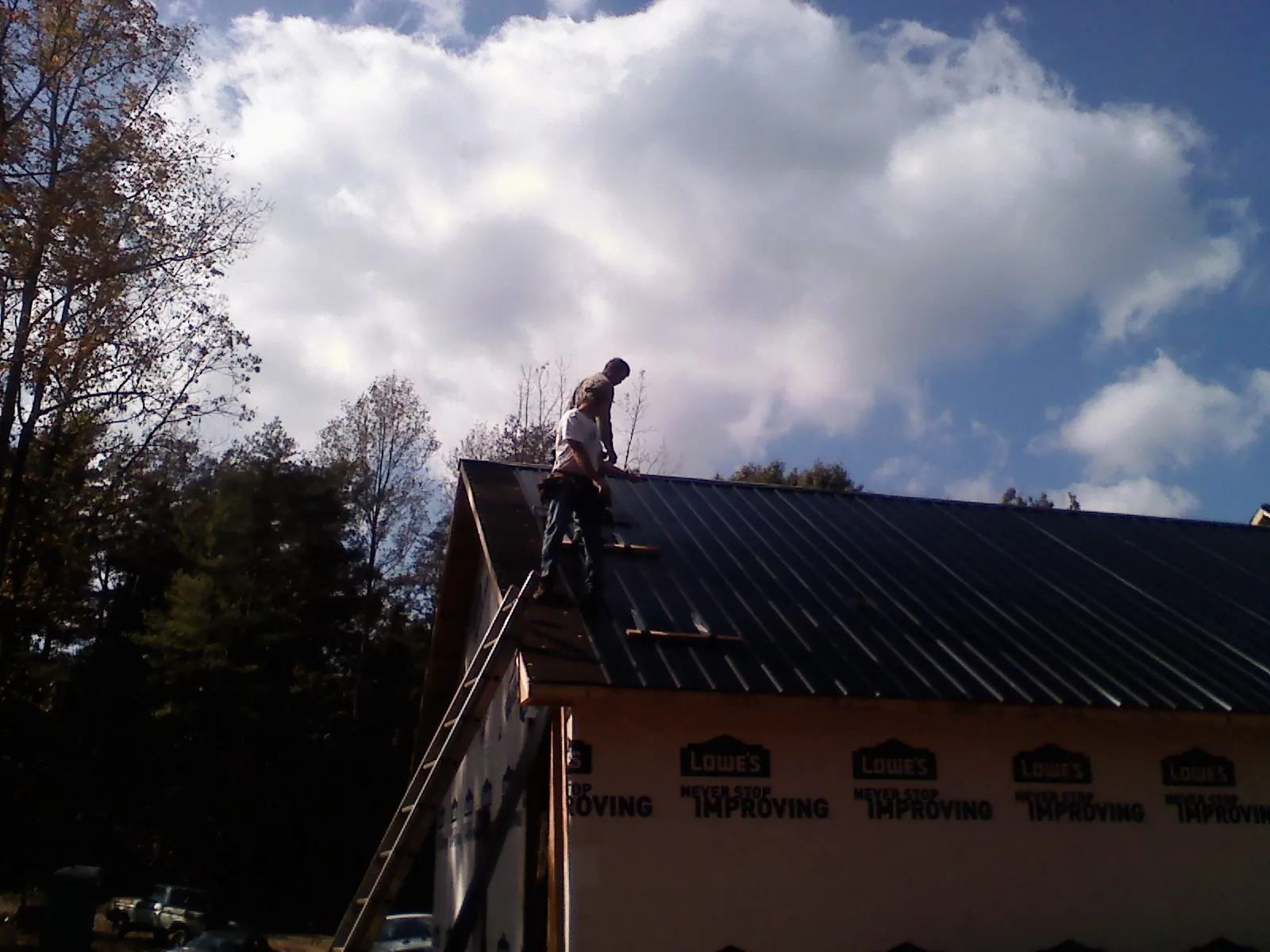 Roofer fastening dark metal panels high against a cloudy sky, from a Roof Inspection job in Elliston