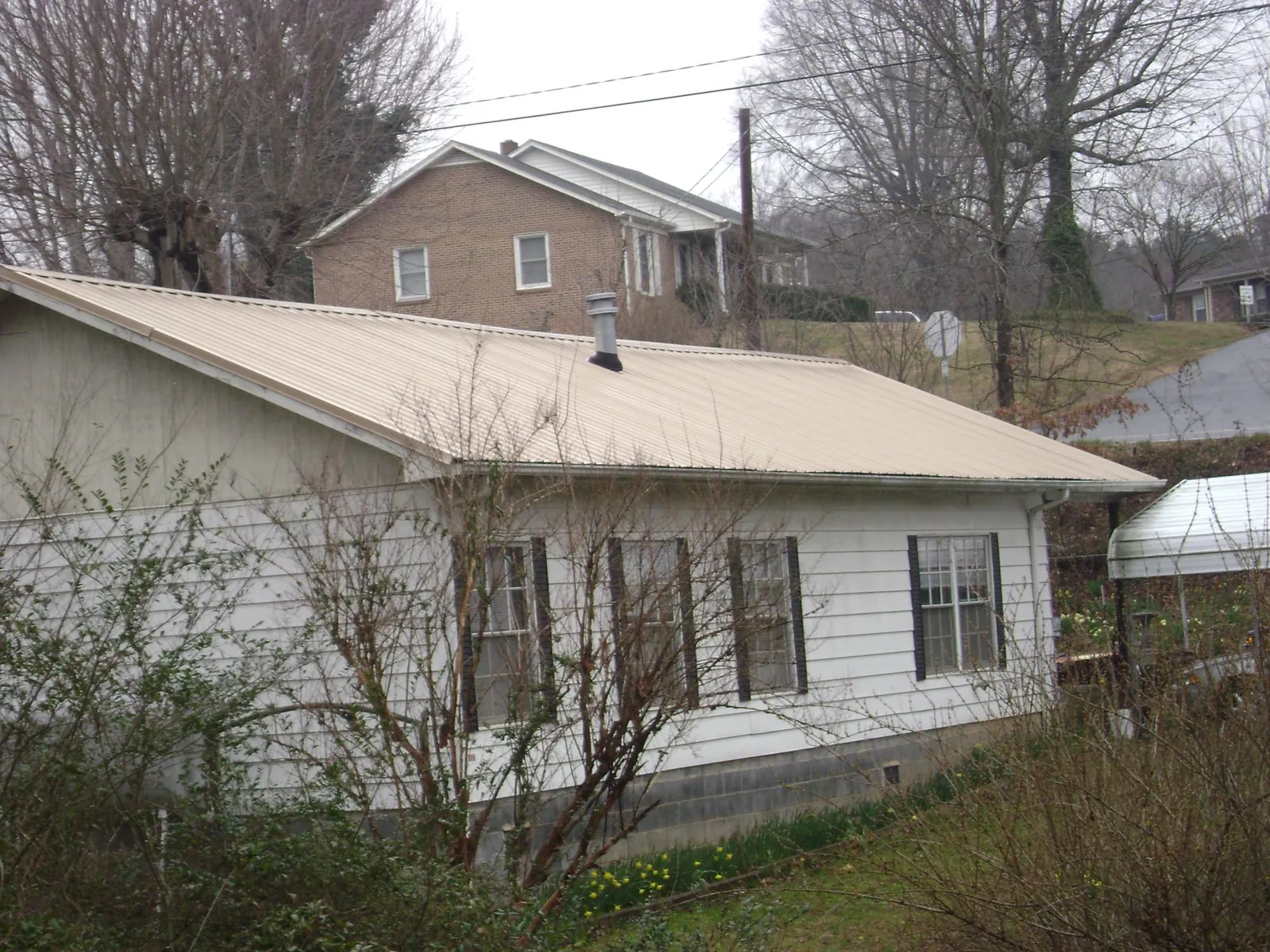 Tan metal roof on a white sided house set into a hillside — Commercial Roofing by Roofing Brothers in Elliston